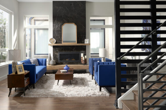 Modern living room with blue sofas, black fireplace, wooden floors, and large windows