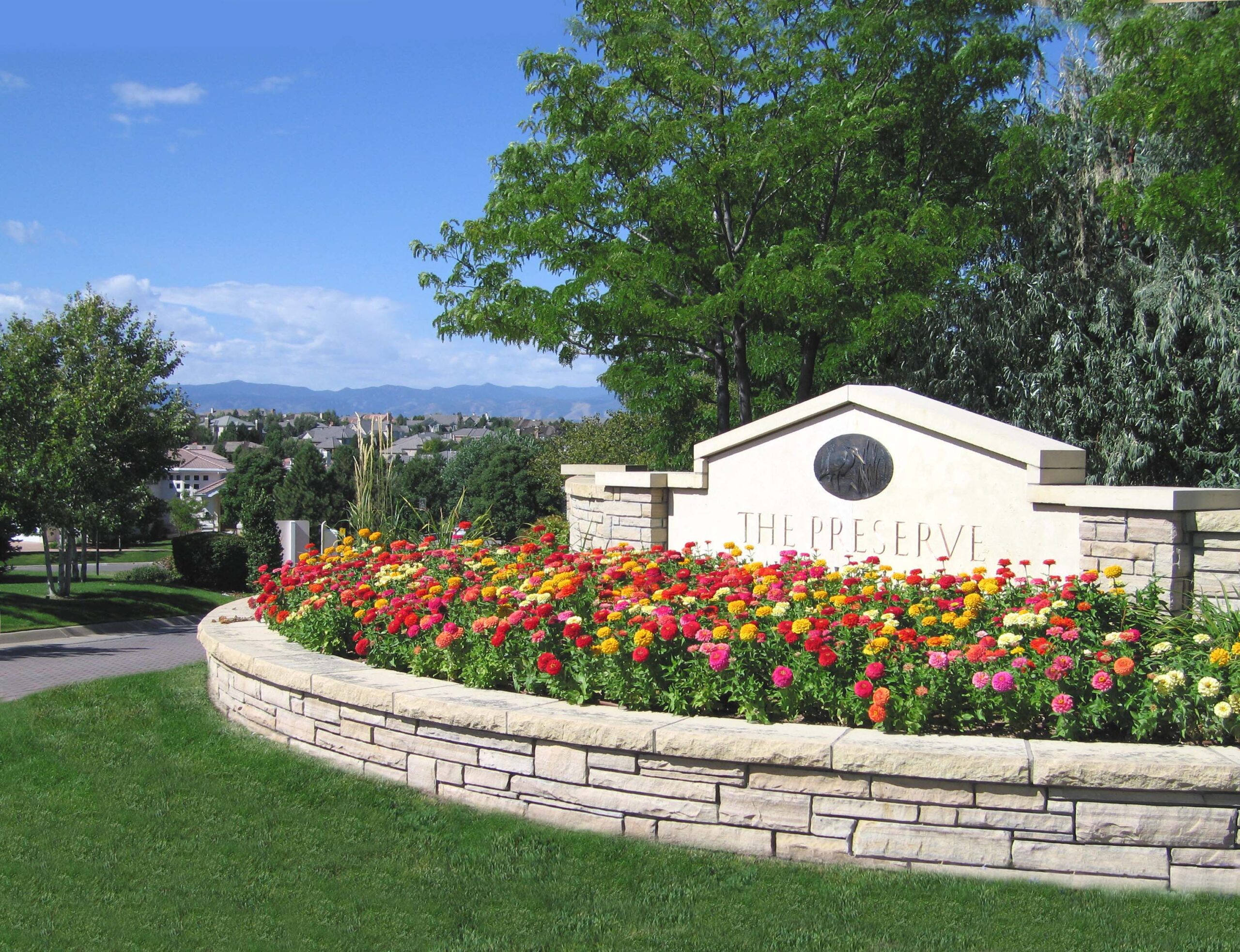 Entrance to The Preserve with a stone sign, colorful flowers, and manicured green grass.