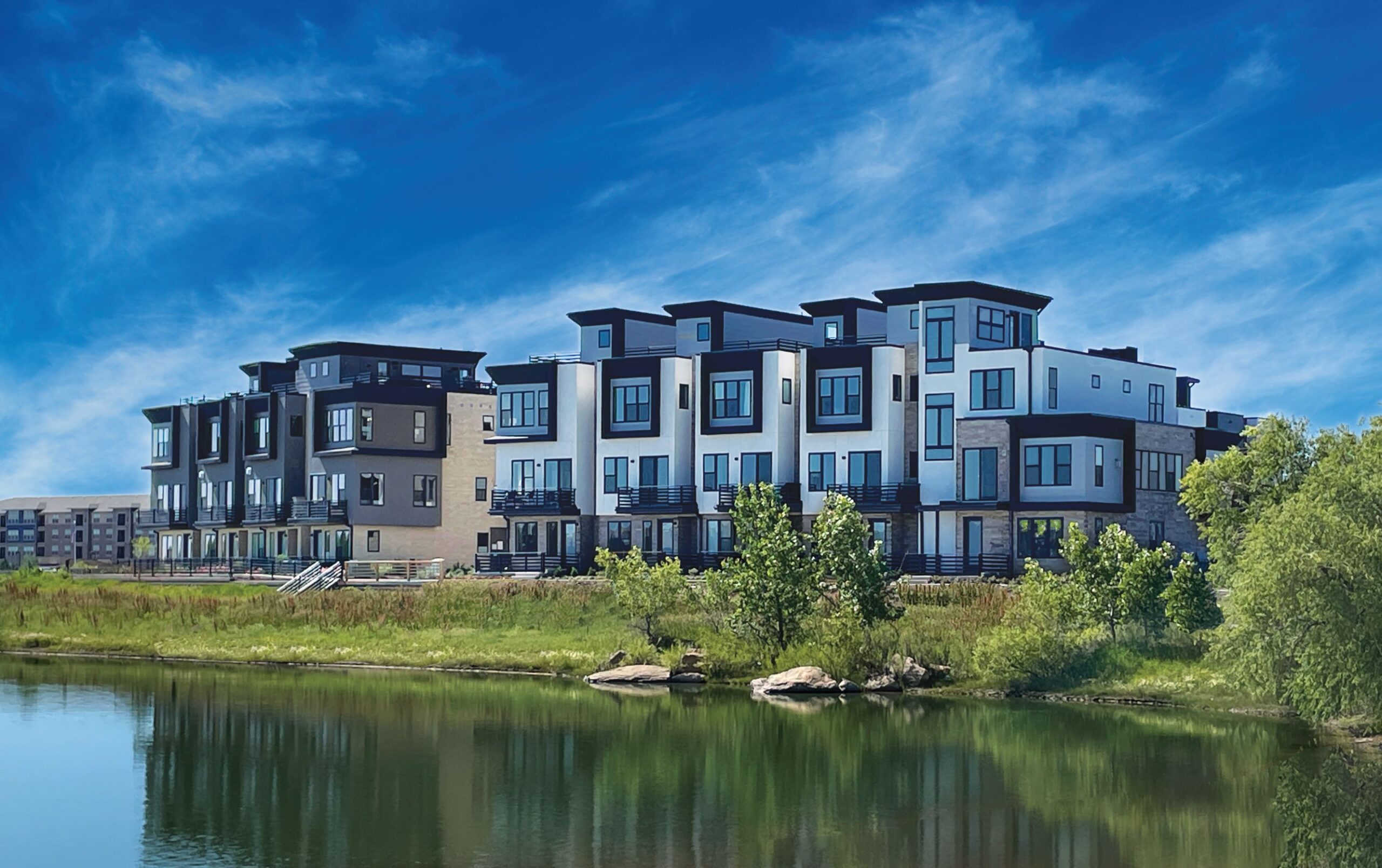 Modern buildings on the northwest side near a pond under a blue, partly cloudy sky